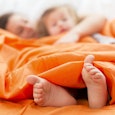 A mother and her daughter hugging each other, while laying in their family bed covered with orange s...
