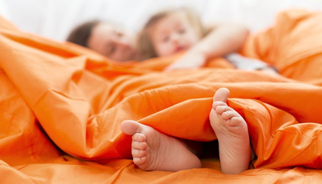 A mother and her daughter hugging each other while lying in their family bed covered with orange she...