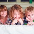 Siblings, two boys and a girl, smiling and lying on a bed in pajamas.