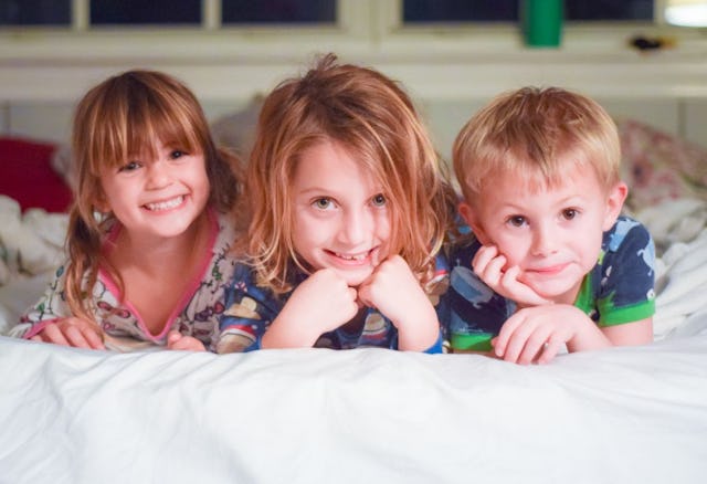 Siblings, two boys, and a girl, smiling and lying on a bed, stomach down in pajamas