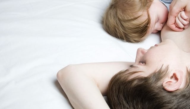 A mother breastfeeding her baby while both are lying on white bed sheets