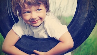 A little boy hanging on a tire while having a big smile on his face