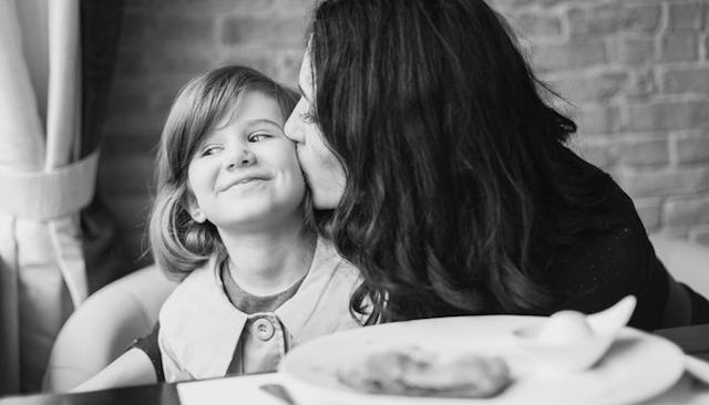 A mother kissing her daughter while having lunch at the table in black and white