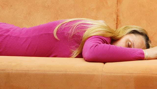 A woman in a pink shirt sleeping stomach down in a horizontal position on an orange couch