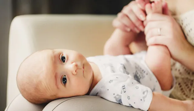 A mother playing with baby in a onesie on her lap