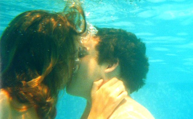 A teenage girl and a teenage boy kissing underwater in a swimming pool