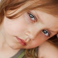 Close-up photo of a sick kid leaning on her hand and looking at the camera