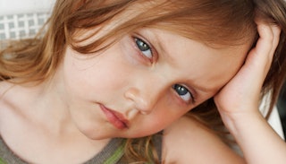A close-up photo of a sick kid leaning on her hand with a neutral facial expression