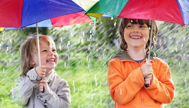 Two boys smiling under colorful umbrellas while it's raining