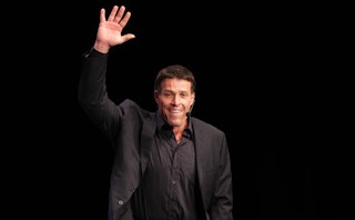 American author Tony Robbins in a black suit and shirt waving with one hand during an event