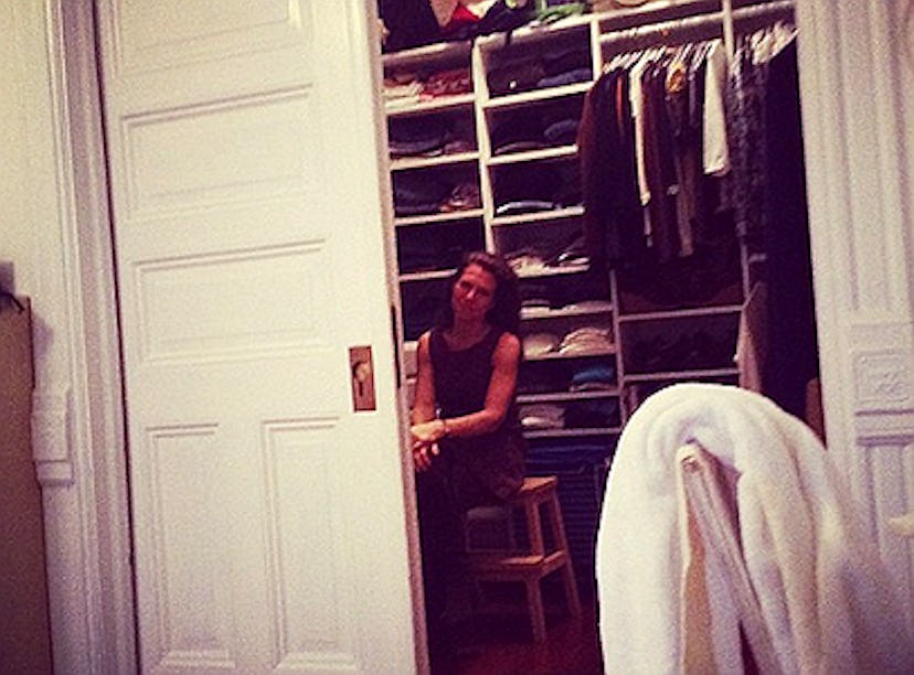 A woman sitting on a chair in her closet with one door opened