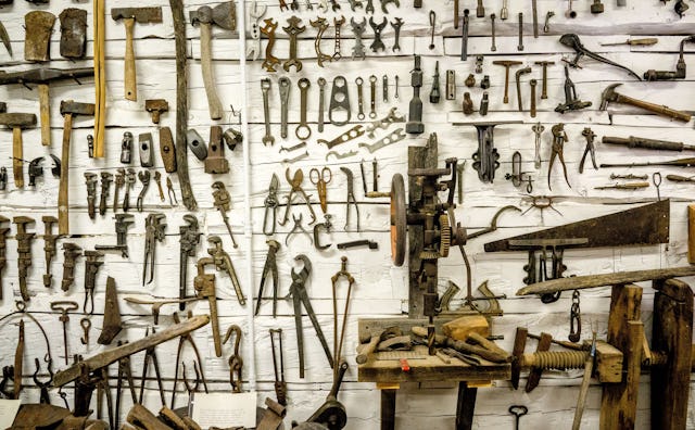 A white wall with tools in various shapes and sized attached to it in a shop class