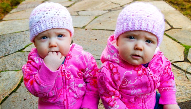 Twin babies wearing pink hoodies and pink beanies sitting