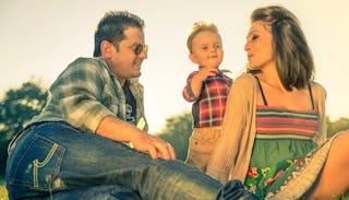 An unmarried mom sitting on the grass next to her partner and her son