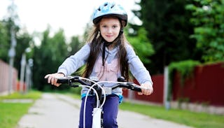 A brown-haired girl with blue eyes, in a blue hoodie with a pink bow, riding a bike down the street 