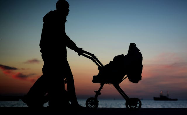 Two parents walking with their baby in a baby cart next to the sea with the sky visible in the backg...