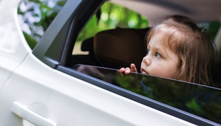A girl with brown hair looking through the window of a white car while being dropped off at school. 
