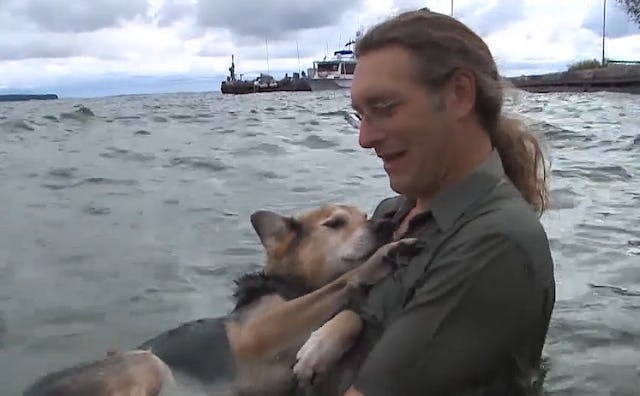 A man holding his ailing dog in water, helping him have fun in the sea.