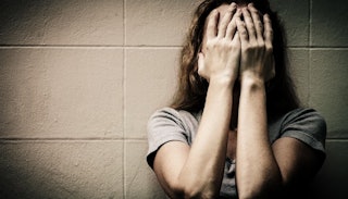 A depressed woman holding her hands over her face while leaning against a wall