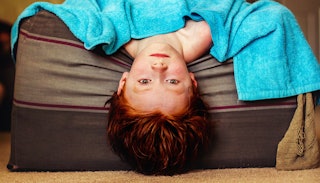  A little boy lying on the bed with his head down, covered with a blue blanket 