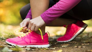  A woman tying her pink sneakers with yellow laces, wearing a burgundy shirt and black tights on her...