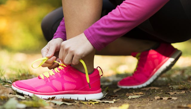 A woman tying her pink sneakers with yellow laces, wearing a burgundy shirt and black tights on her...