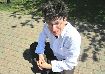 James Altucher wearing a white shirt, black pants and glasses while crouching on concrete tiles