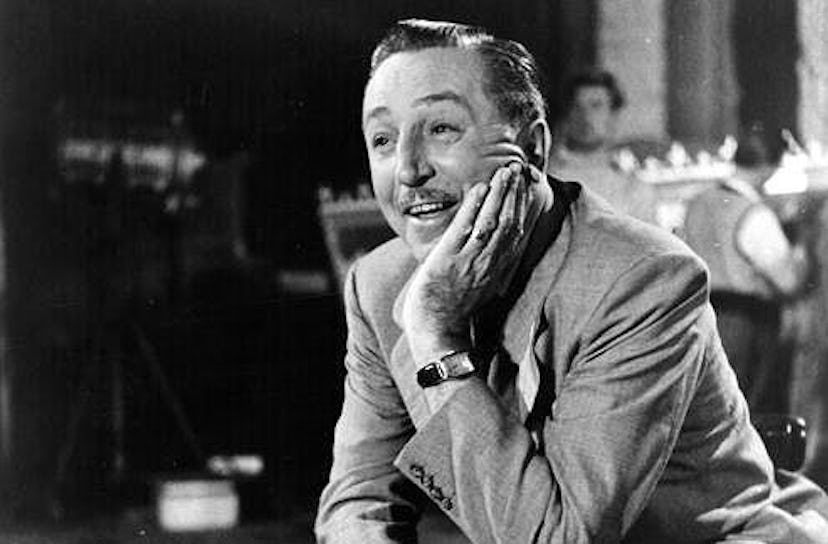 Walt Disney wearing a suit and a watch while leaning on a table in a black and white photo