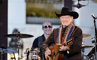 Willie Nelson wearing a cowboy hat and holding a guitar while playing with a band on stage