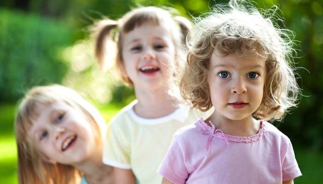 Three girls wearing pink and yellow shirts and smiling with a blurred background on a playdate