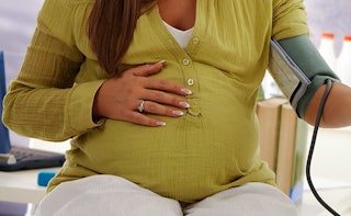 A pregnant woman at 40 in an olive linen shirt sitting and her hand is on her belly