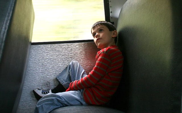 A boy with anxiety in a red long-sleeved shirt with gray stripes and blue denim jeans sitting in a s...