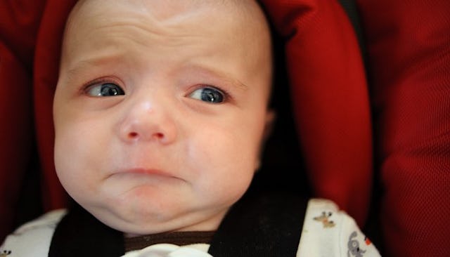 A colicky baby sitting in a baby car seat and crying