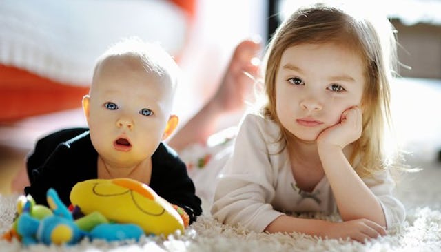 A blonde toddler holding a toy and a girl in a pink shirt next to him lying on their stomachs