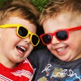 Two boys laying on the grass, one with red sunglasses on and the other with yellow sunglasses on 