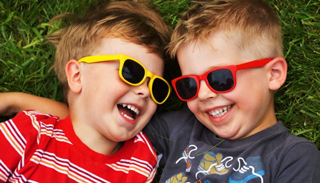 A boy in a striped red shirt and yellow sunglasses lying and smiling next to a boy in a blue shirt a...