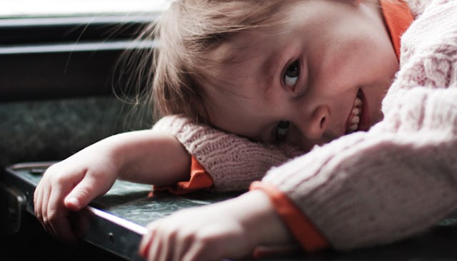 A brown-haired child in a beige sweater and orange shirt lying face-down and smiling
