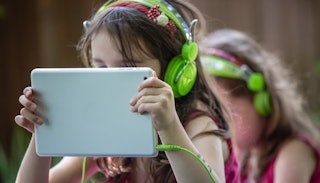 Two girls looking at their tablets with green earphones on their heads during their screen time