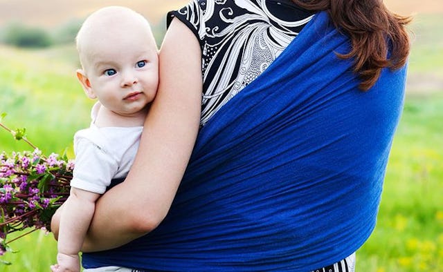 A close-up of a hippie mum holding her baby in front of her while wrapped in a blue scarf
