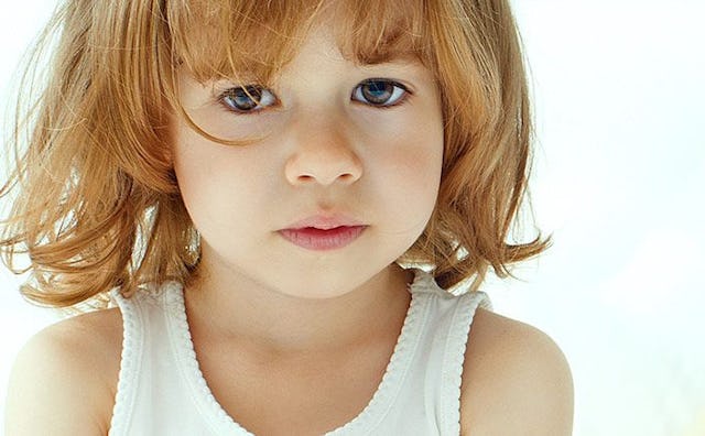 A small and young blonde child with brown eyes in a white tank top