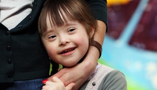 A girl with Down Syndrome smiling while hugging her mum