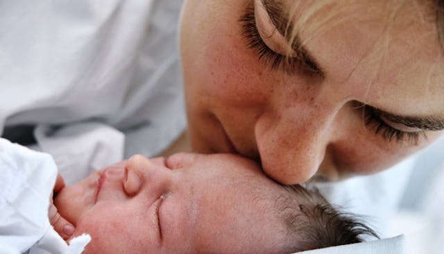 A mother in a white shirt kissing her newborn baby on the chin after giving one up