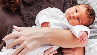 A newborn baby lying down on her parent's arm