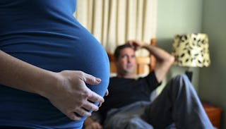 Pregnant wife standing and a husband sitting on a couch in the background 