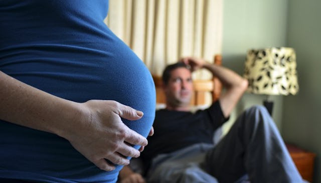 Pregnant wife standing and a husband sitting on a couch in the background