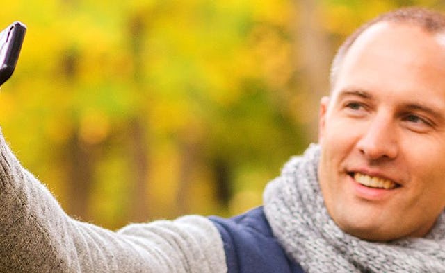 A middle-aged man in a blue-beige jacket smiling and taking a selfie for Tinder