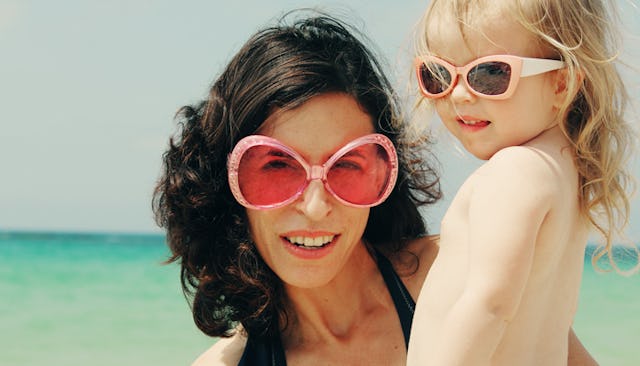A mom and her daughter on a beach wearing sunglasses.