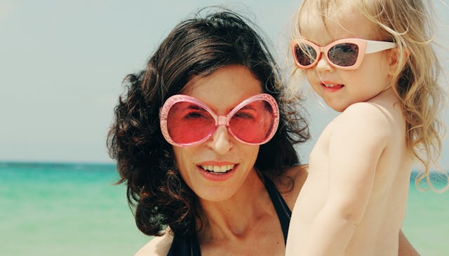 A mom and her daughter on a beach wearing sunglasses. 