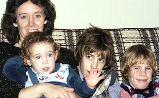 A mother sitting on the sofa with her three kids while posing for a photo in the '80s