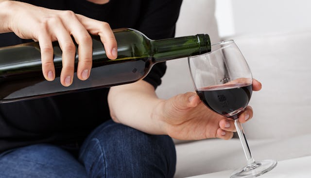 A close-up of a woman pouring herself a glass of wine in a black shirt and blue denim jeans